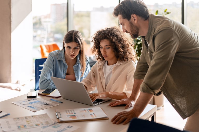 Three colleagues collaborating on a project analyzing data on a laptop in a modern office